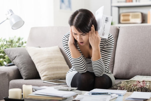 woman sitting on the couch looking surprised while checking utility bills
