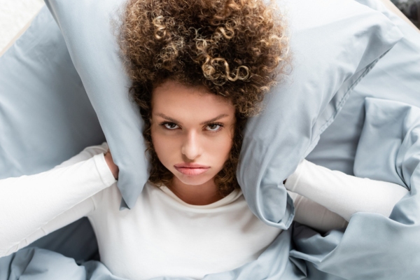 woman covering her ears with pillow on the bed due to noisy window air conditioner