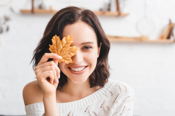 woman holding autumn leaf on eye depicting end of summer