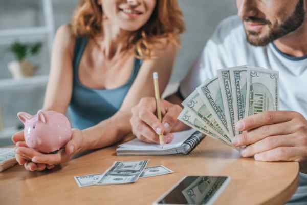 Cropped image of a couple discussing fuel expenses with piggy bank and dollars on hand depicting generator fuel