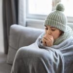 woman wrapped in blanket and wearing scarf & beanie indoors due to heating issues at home