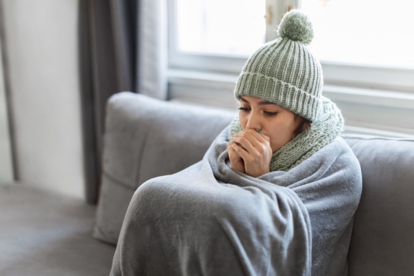 woman wrapped in blanket and wearing scarf & beanie indoors due to heating issues at home