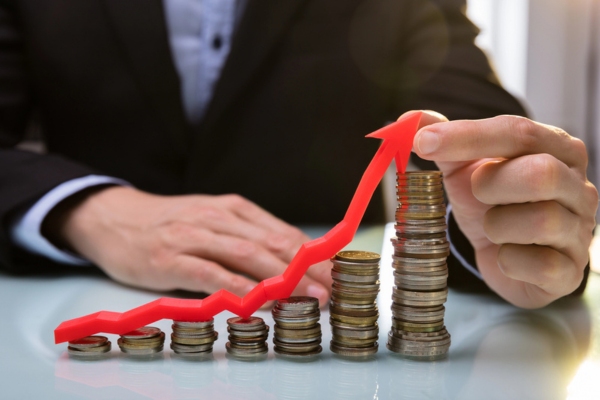 man holding red arrow on top of increasing gold coins depicting inflation and currency fluctuation